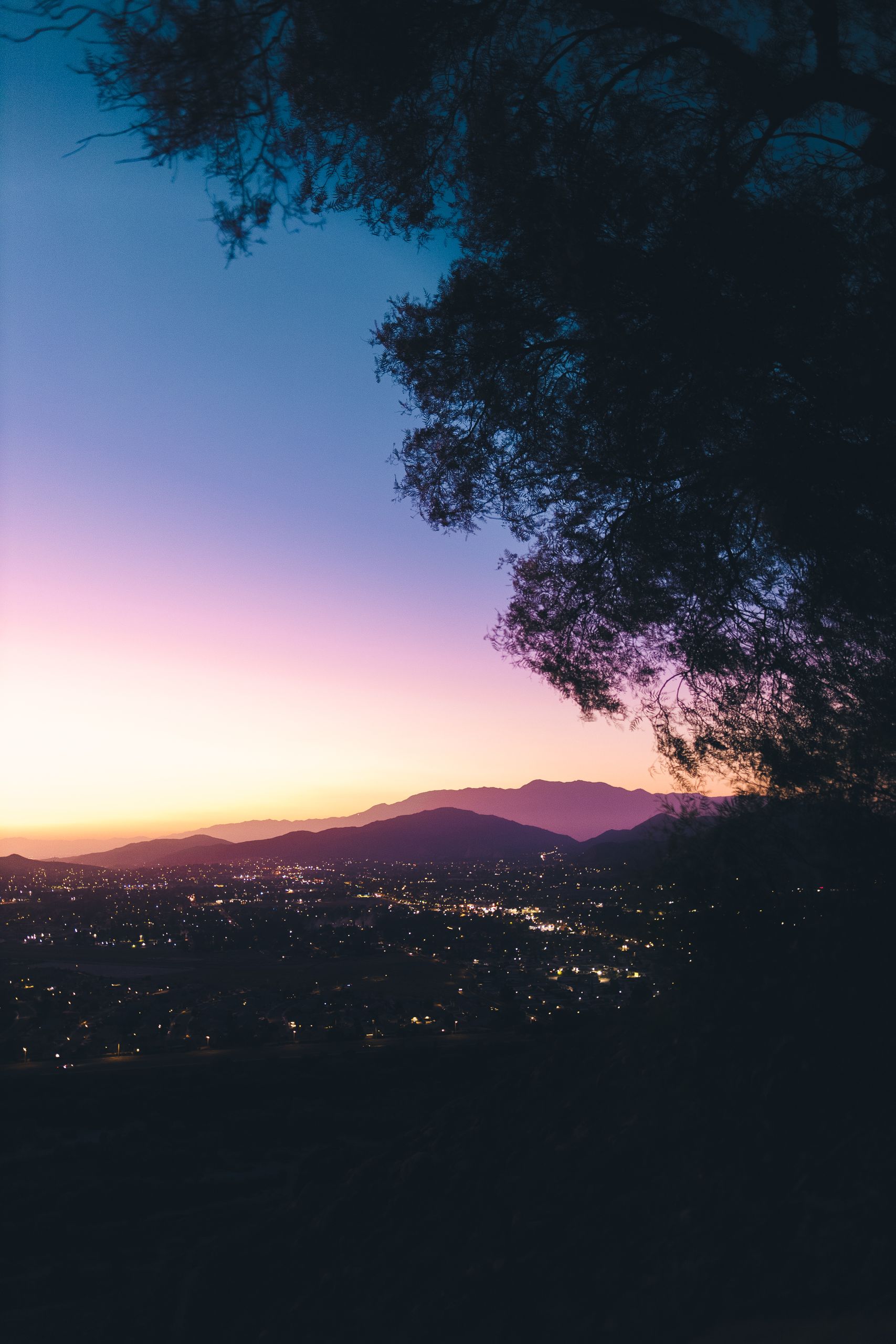 A breathtaking sunset view over a city with mountains and silhouetted trees, capturing the magic of twilight.